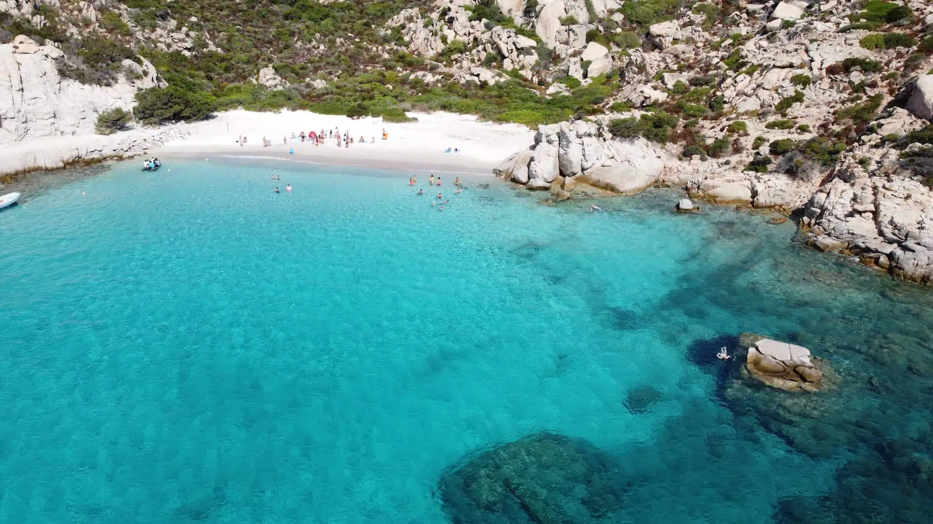 A breathtaking aerial view of a secluded cove with turquoise waters, a white sandy beach, and rugged cliffs covered in greenery.