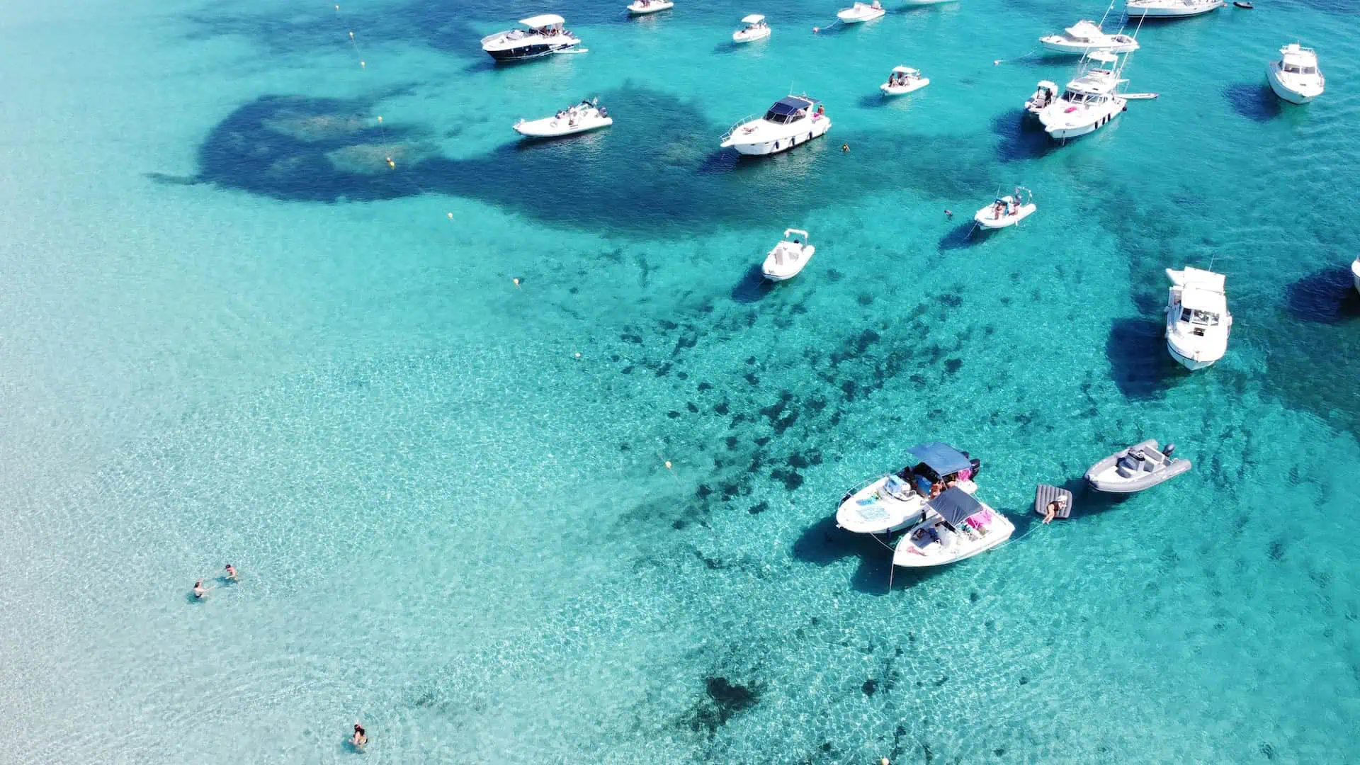 A breathtaking aerial shot of a pristine white sand beach, turquoise waters, and anchored boats near a lush coastal landscape.