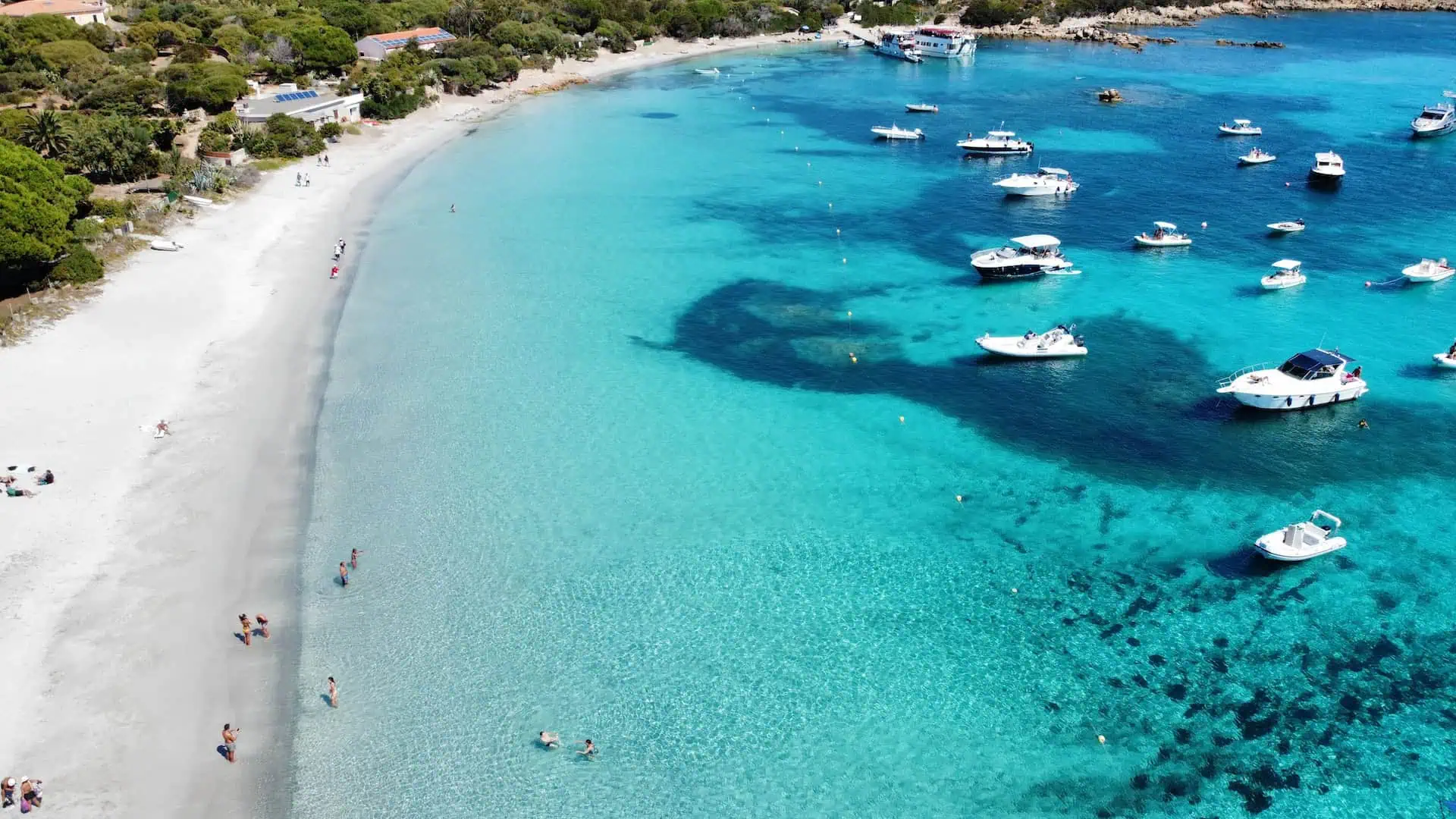 A breathtaking aerial shot of a pristine white sand beach, turquoise waters, and anchored boats near a lush coastal landscape.