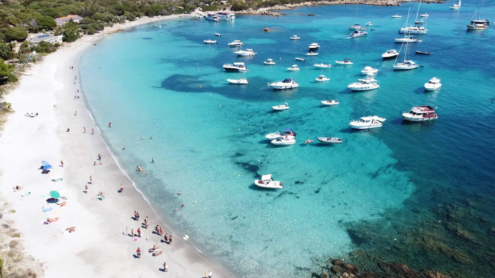 A breathtaking aerial shot of a pristine white sand beach, turquoise waters, and anchored boats near a lush coastal landscape.