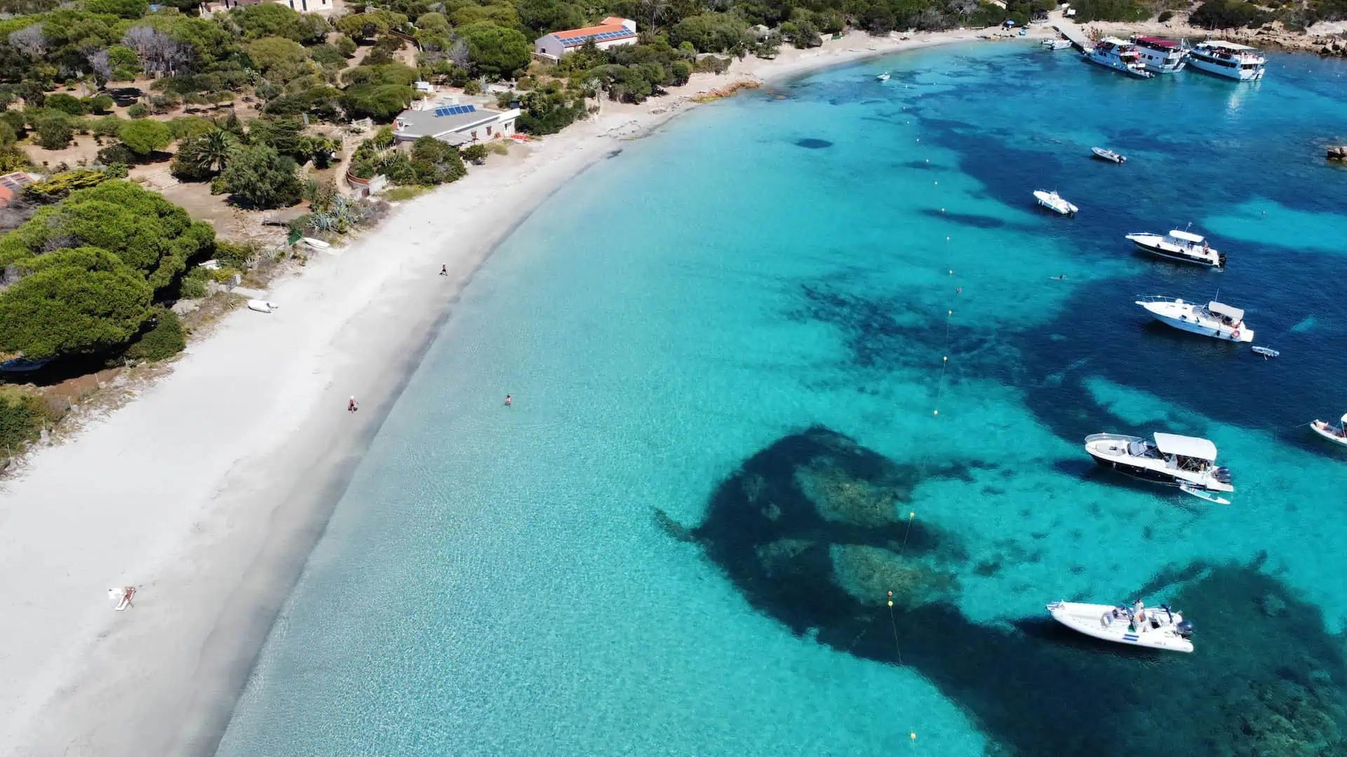 A breathtaking aerial shot of a pristine white sand beach, turquoise waters, and anchored boats near a lush coastal landscape.