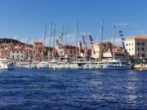 A marina with multiple sailboats docked in front of a colorful coastal town under a clear blue sky.